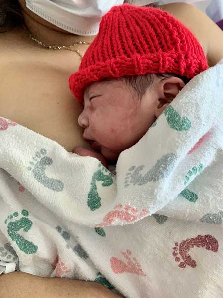 Allison-Hernandez Mother Embracing Newborn Child With a Red Hat